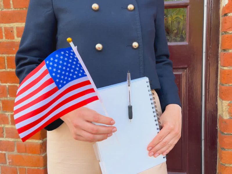 Devojka kulturno obučena drži zastavu Amerike u ruci i svesku sa hemijskom